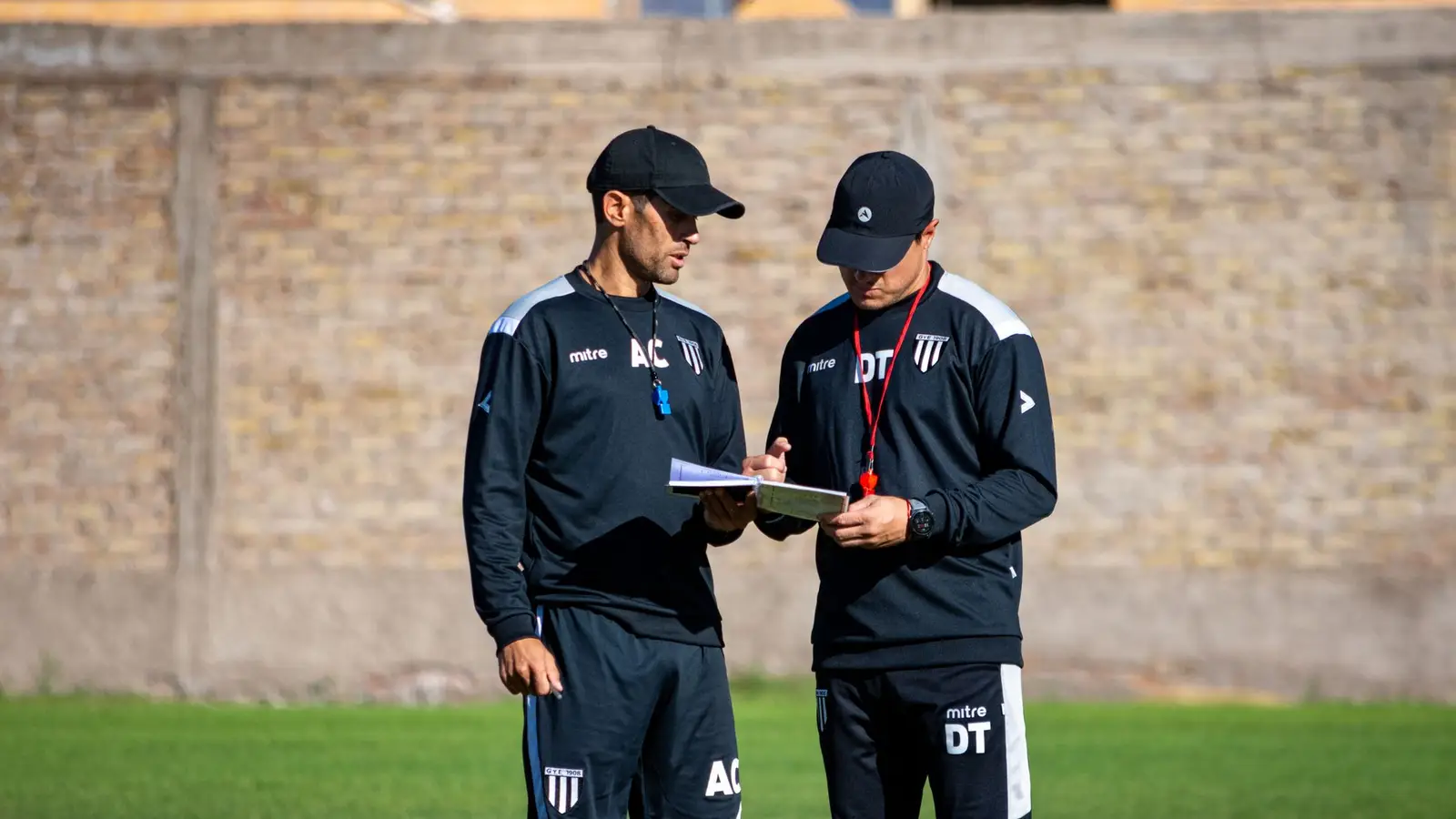 Two football coaches reviewing notes on a clipboard on the pitch